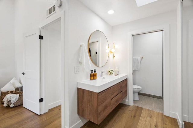 bathroom with vanity, hardwood / wood-style floors, a skylight, and toilet