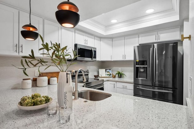 kitchen with decorative light fixtures, a raised ceiling, white cabinetry, stainless steel appliances, and light stone countertops