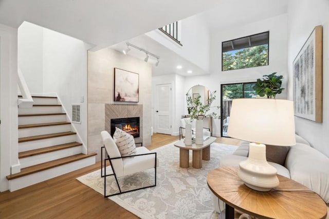 living room featuring track lighting, a fireplace, light hardwood / wood-style flooring, and a high ceiling