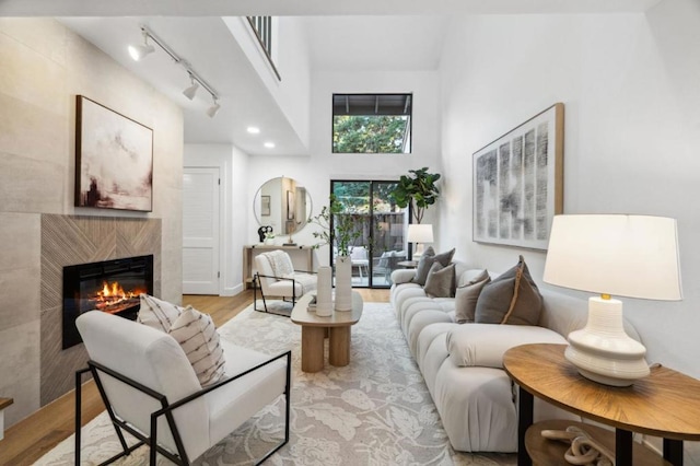 living room featuring a towering ceiling, a high end fireplace, rail lighting, and light wood-type flooring