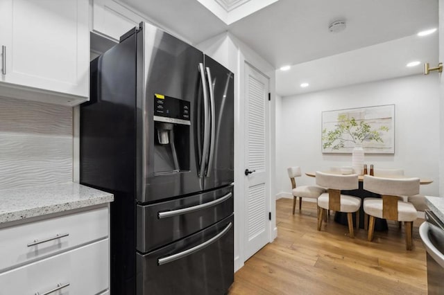 kitchen featuring white cabinetry, stainless steel fridge, light hardwood / wood-style floors, and light stone counters