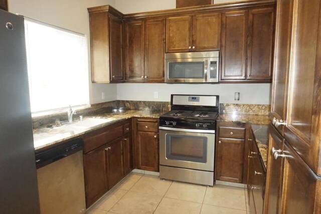 kitchen with dark stone countertops, stainless steel appliances, sink, and light tile patterned floors