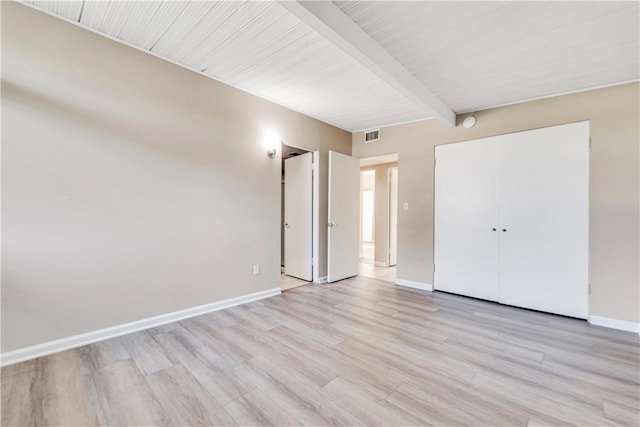 unfurnished bedroom featuring beamed ceiling, a closet, and light hardwood / wood-style flooring