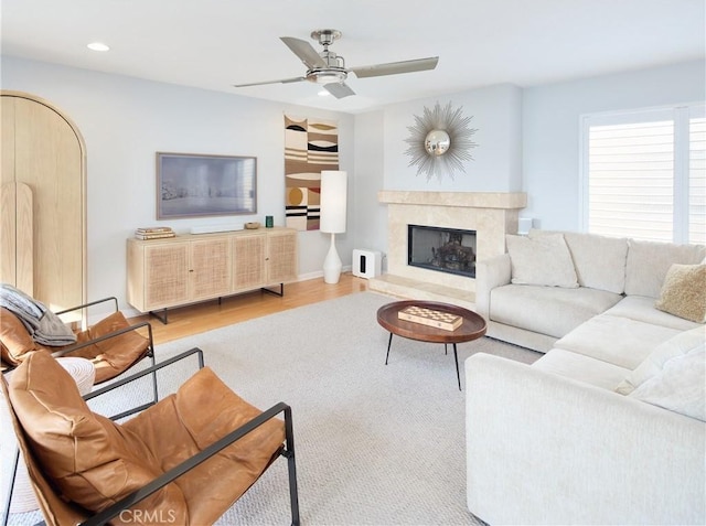 living room with a high end fireplace, light hardwood / wood-style floors, and ceiling fan