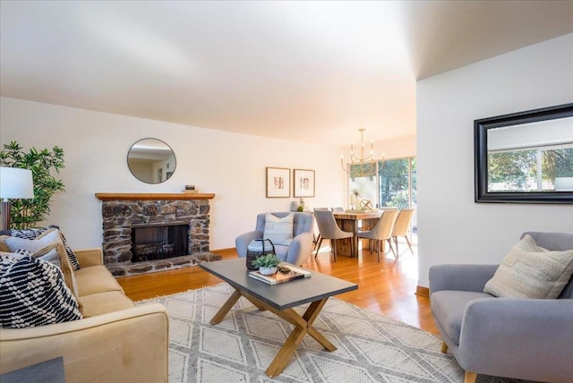 living room featuring a stone fireplace, a notable chandelier, and light hardwood / wood-style flooring