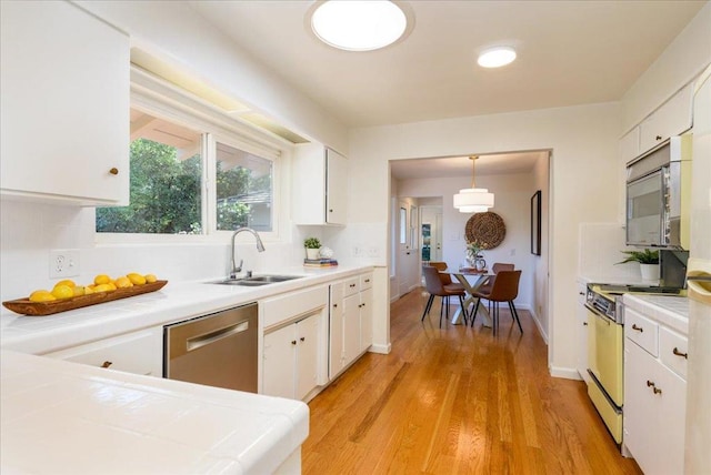 kitchen with white cabinetry, dishwasher, sink, hanging light fixtures, and range