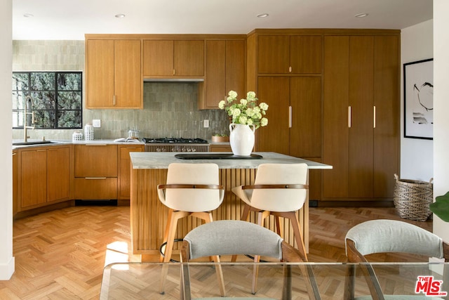 kitchen with sink, light parquet flooring, a kitchen island, decorative backsplash, and stainless steel gas stovetop