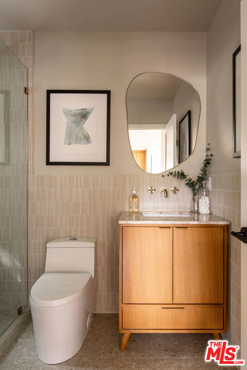 bathroom with vanity, toilet, an enclosed shower, and tile walls