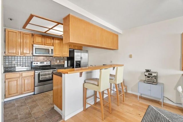 kitchen featuring hardwood / wood-style flooring, a breakfast bar area, appliances with stainless steel finishes, backsplash, and kitchen peninsula