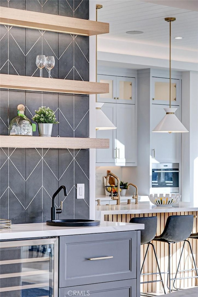 bar with wine cooler, sink, gray cabinetry, and stainless steel oven