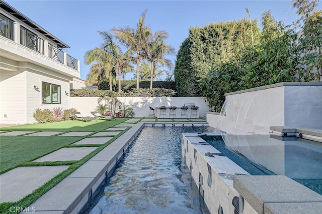 view of swimming pool featuring pool water feature, a yard, and a bar