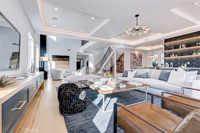 living room with a raised ceiling, a chandelier, and light hardwood / wood-style flooring