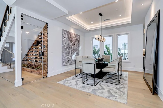 dining room with an inviting chandelier, light hardwood / wood-style flooring, and a raised ceiling