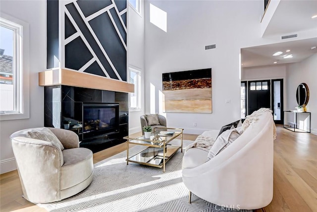 living room featuring a towering ceiling, a tiled fireplace, and light hardwood / wood-style floors