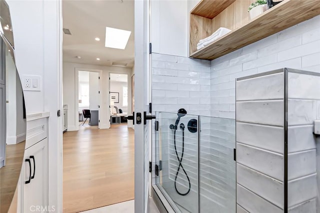 bathroom featuring hardwood / wood-style flooring, walk in shower, decorative backsplash, and a skylight