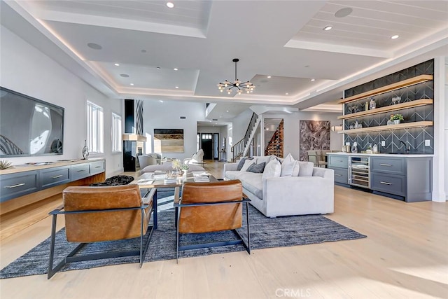 living room featuring light hardwood / wood-style flooring, bar, a notable chandelier, a tray ceiling, and beverage cooler