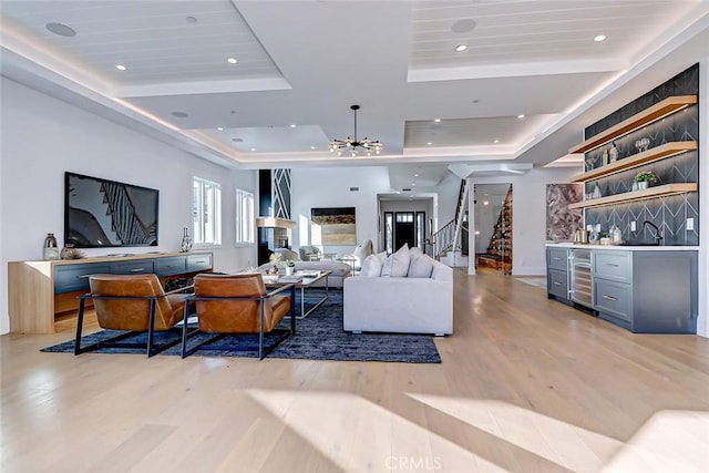 living room featuring a raised ceiling, wet bar, a notable chandelier, and light hardwood / wood-style flooring