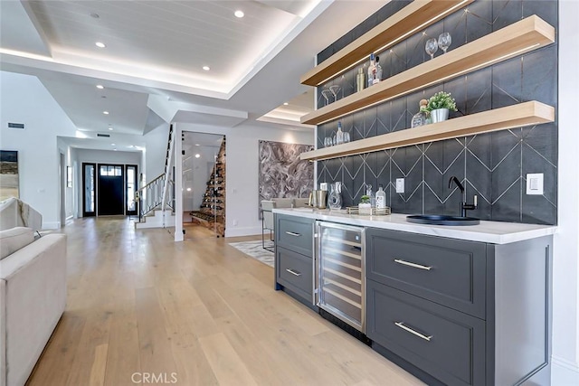 bar with sink, gray cabinets, decorative backsplash, beverage cooler, and light wood-type flooring