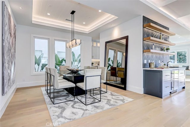 dining space featuring bar, a tray ceiling, and light wood-type flooring