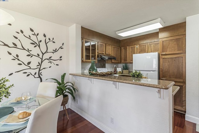 kitchen with dark hardwood / wood-style flooring, a kitchen breakfast bar, kitchen peninsula, and white fridge