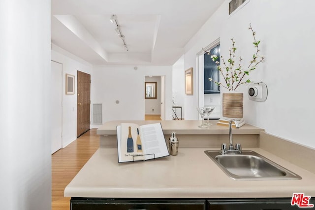 kitchen featuring a raised ceiling, rail lighting, sink, and light hardwood / wood-style flooring