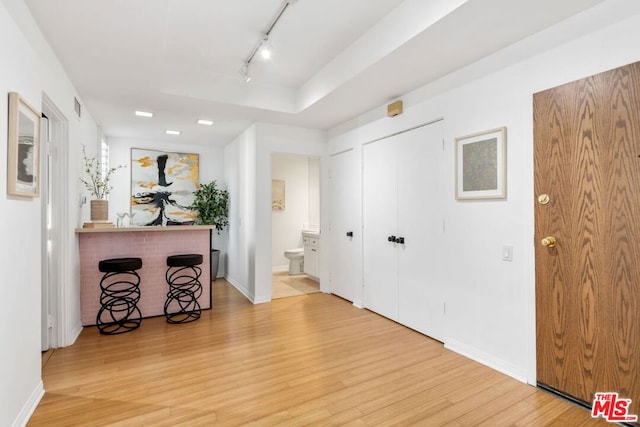 interior space featuring a raised ceiling, rail lighting, and light wood-type flooring