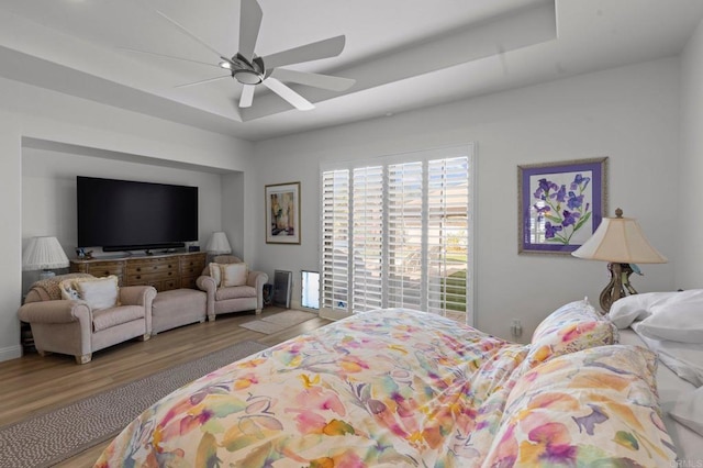 bedroom with ceiling fan, a tray ceiling, and hardwood / wood-style floors