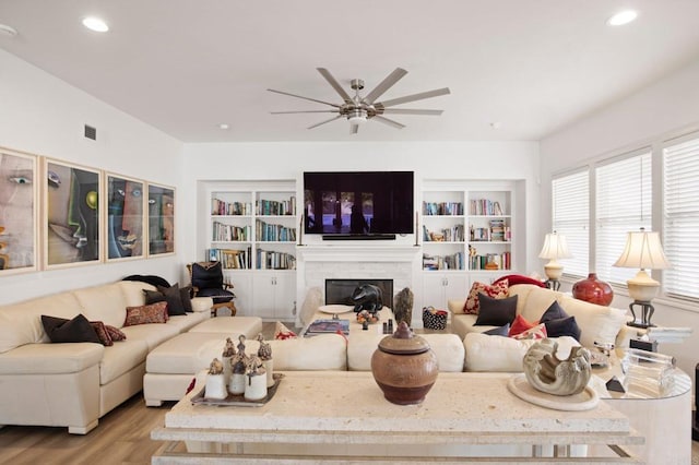 living room with built in features, light hardwood / wood-style floors, and ceiling fan