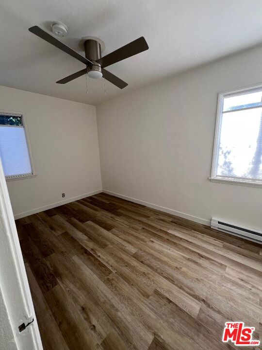 empty room with ceiling fan, hardwood / wood-style floors, and a baseboard heating unit