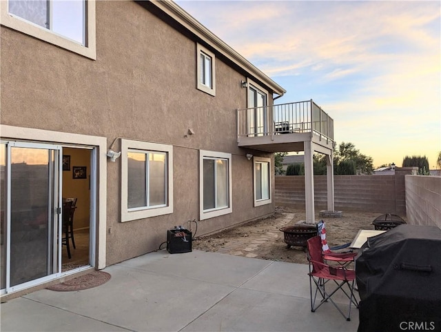 back house at dusk featuring a balcony, a patio area, and a fire pit