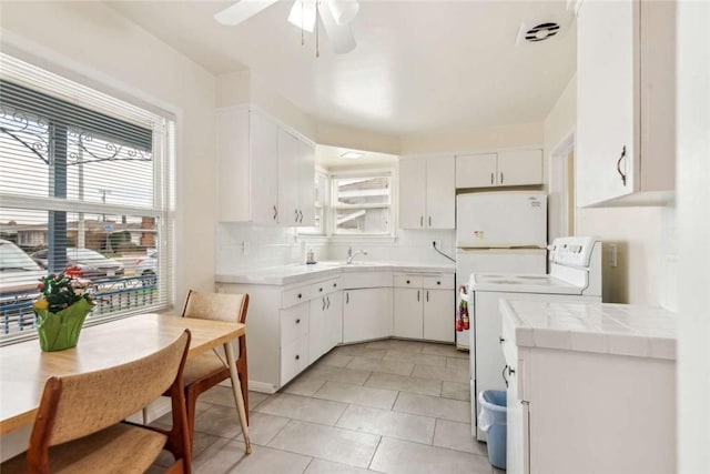 kitchen featuring backsplash, tile counters, washer / dryer, and white cabinets