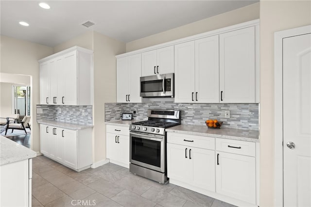 kitchen with light tile patterned floors, white cabinetry, stainless steel appliances, light stone counters, and decorative backsplash