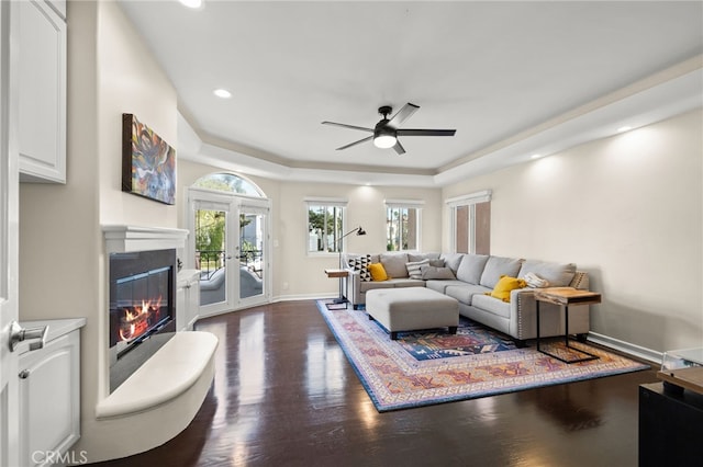 living room with dark wood-type flooring, ceiling fan, a raised ceiling, and french doors