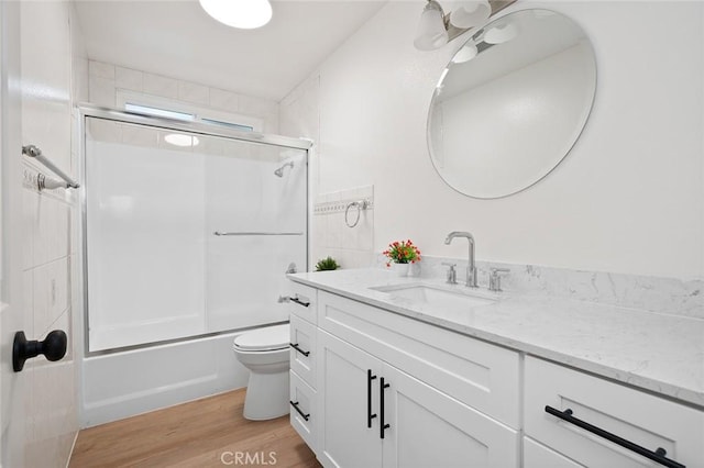 full bathroom featuring vanity, hardwood / wood-style floors, shower / bath combination with glass door, and toilet