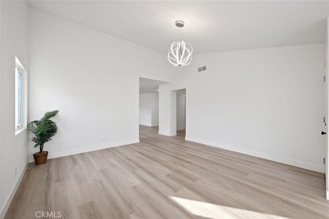 empty room with high vaulted ceiling, light hardwood / wood-style floors, and a chandelier