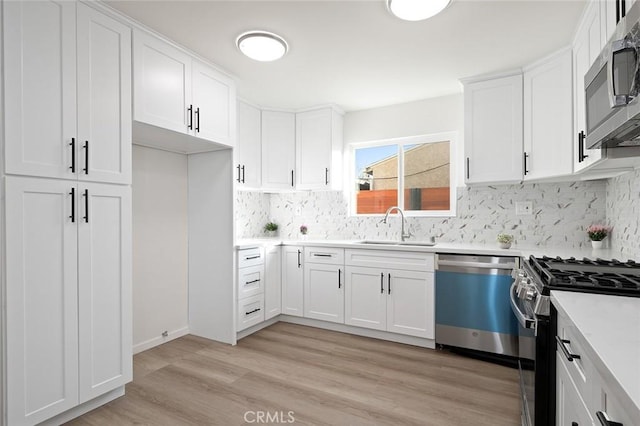 kitchen with appliances with stainless steel finishes, sink, white cabinets, and light hardwood / wood-style floors