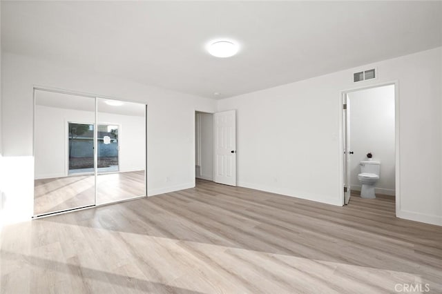 unfurnished bedroom featuring ensuite bathroom, light hardwood / wood-style floors, and a closet