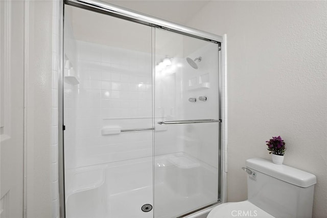 bathroom featuring a shower with door and toilet