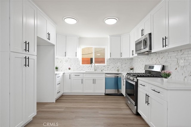 kitchen with white cabinetry, sink, decorative backsplash, stainless steel appliances, and light wood-type flooring