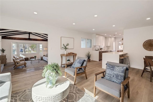 living area with light wood-style floors, baseboards, beamed ceiling, and recessed lighting