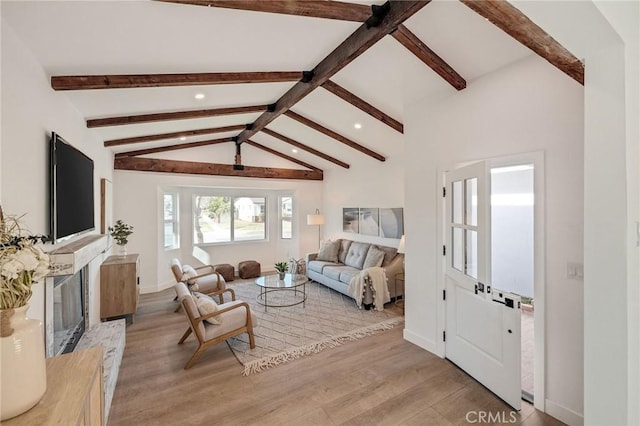 living area featuring a fireplace with raised hearth, lofted ceiling with beams, baseboards, and wood finished floors