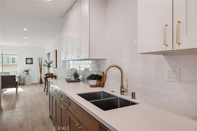 kitchen with light countertops, backsplash, light wood-style floors, white cabinetry, and a sink