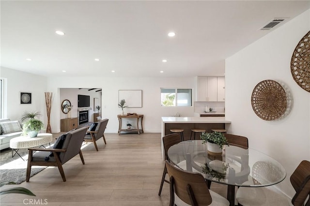 dining room with light wood finished floors, a glass covered fireplace, visible vents, and recessed lighting