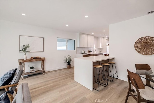 kitchen featuring light countertops, visible vents, light wood-style flooring, white cabinetry, and a kitchen breakfast bar