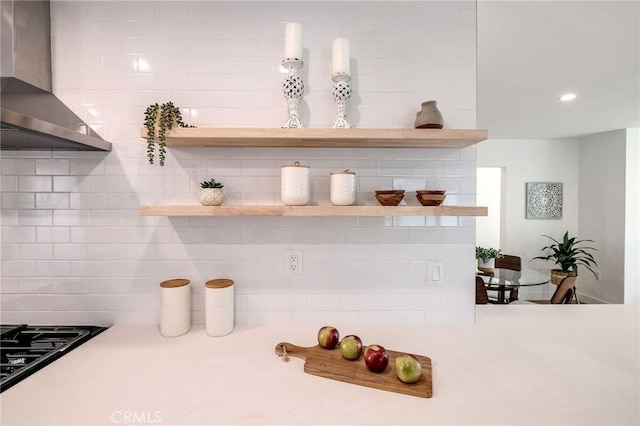 room details featuring wall chimney exhaust hood, open shelves, light countertops, and decorative backsplash