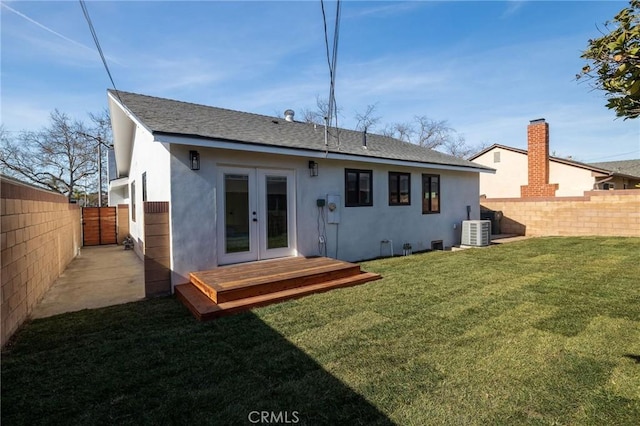 rear view of property with french doors, stucco siding, a lawn, central AC unit, and a fenced backyard