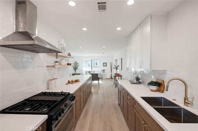 kitchen with sink, white cabinetry, gas range oven, wall chimney exhaust hood, and light wood-type flooring