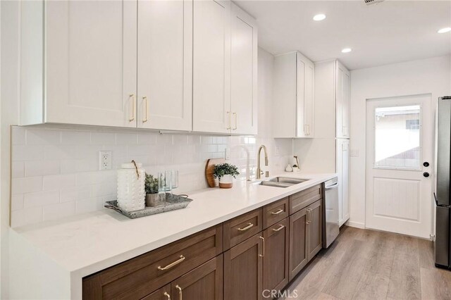 kitchen with sink, appliances with stainless steel finishes, backsplash, light hardwood / wood-style floors, and white cabinets