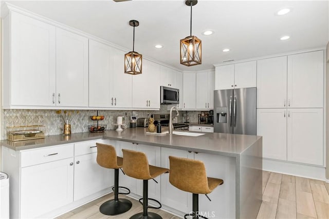 kitchen featuring white cabinetry, appliances with stainless steel finishes, a breakfast bar area, and decorative light fixtures