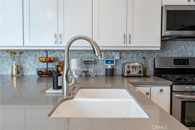 kitchen with sink, white cabinetry, light stone counters, stainless steel appliances, and backsplash